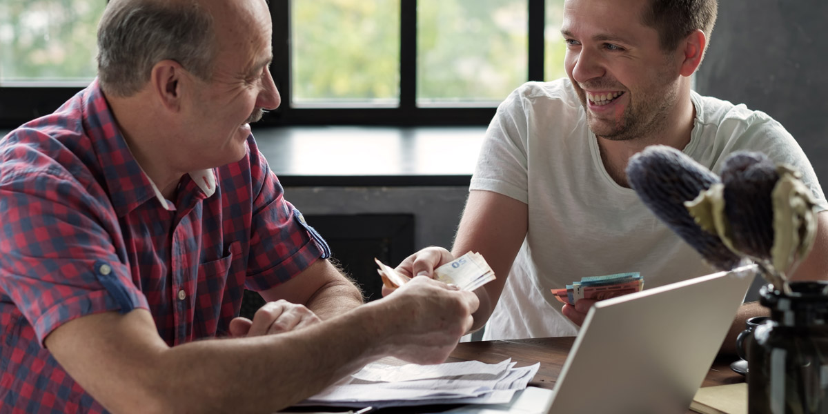 Father handing adult son cash to represent a gift or loan.